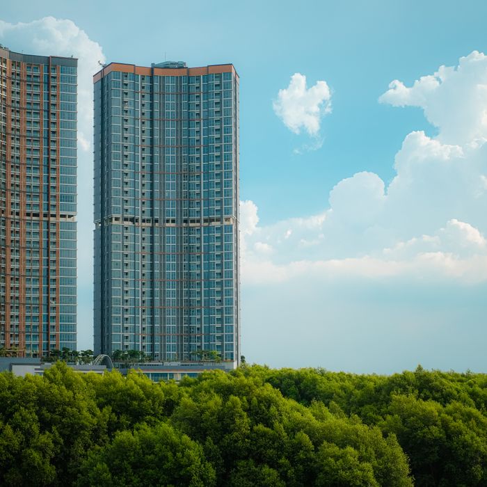 Modern skyscrapers rise above lush greenery against a bright blue sky.