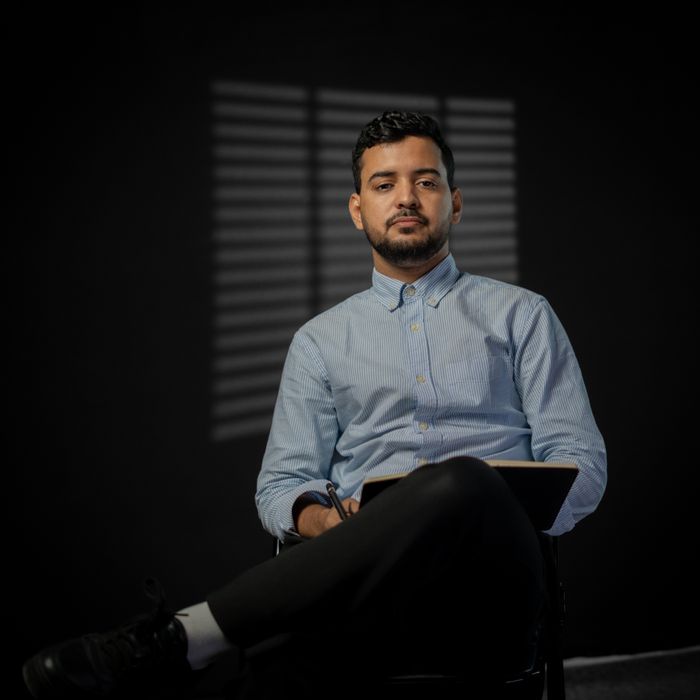 Portrait of a confident businessman seated indoors in a dark, moody setting, holding a notebook.
